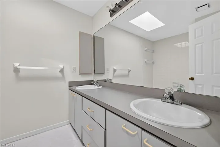 Full bath featuring a skylight, double vanity, a tile shower, and light tile patterned floors