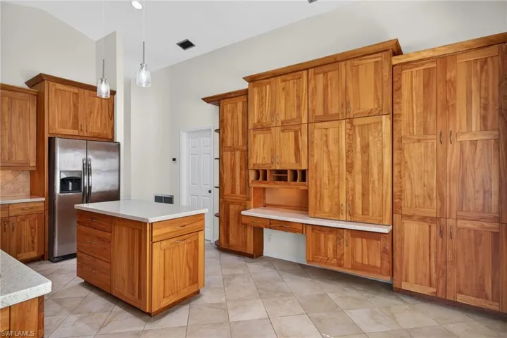 Kitchen with built in desk, a kitchen island, wood finish cabinetry, stainless steel fridge, and hanging light fixtures