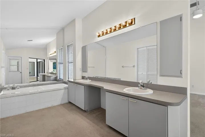 Bathroom featuring light carpet, a garden tub, double vanity, a closet, and lofted ceiling