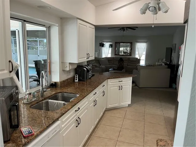 Kitchen featuring dark stone counters, white cabinets, ceiling fan, and sink