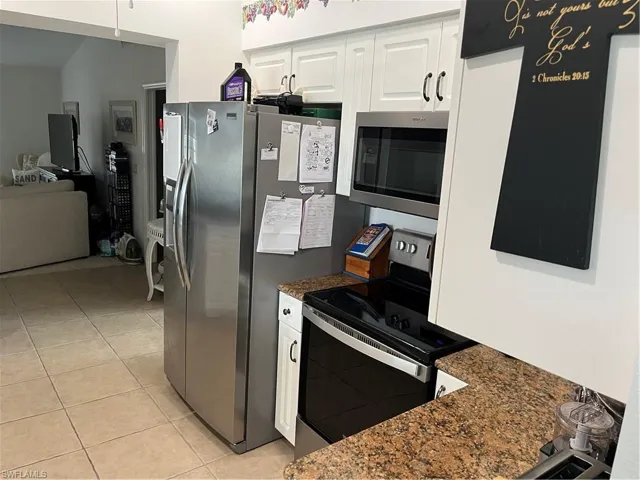 Kitchen featuring appliances with stainless steel finishes, dark stone counters, light tile patterned floors, and white cabinets