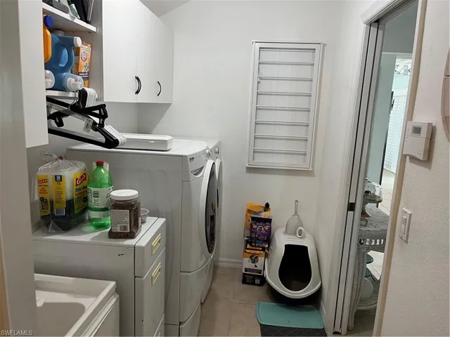 Washroom with separate washer and dryer, light tile patterned flooring, and cabinets