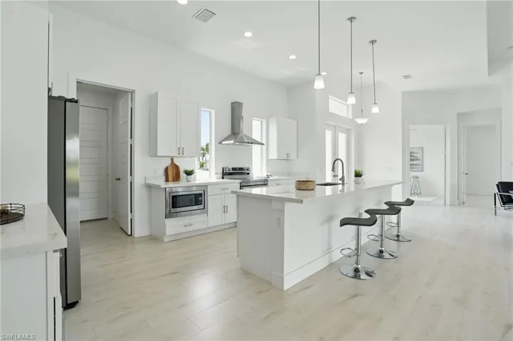 Kitchen with appliances with stainless steel finishes, wall chimney range hood, a sink, white cabinetry, and light wood-type flooring