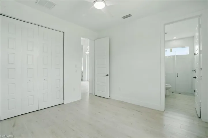 Unfurnished bedroom with wood finished floors, a closet, ensuite bathroom, and baseboards