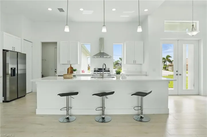 Kitchen featuring stainless steel fridge with ice dispenser, wall chimney range hood, a sink, a kitchen bar, and a towering ceiling
