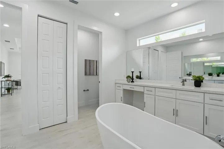 Full bathroom with a closet, a soaking tub, vanity, wood finished floors, and recessed lighting