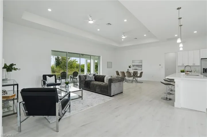 Living area with a raised ceiling, a ceiling fan, light wood-style floors, recessed lighting, and baseboards
