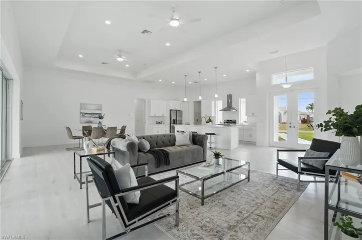 Living area featuring a tray ceiling, ceiling fan, french doors, a towering ceiling, and light wood-style flooring
