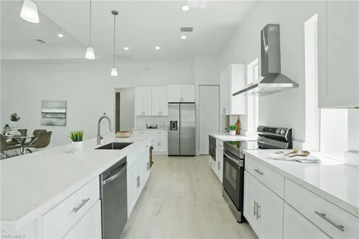 Kitchen featuring appliances with stainless steel finishes, wall chimney exhaust hood, a sink, light wood-style floors, and white cabinetry