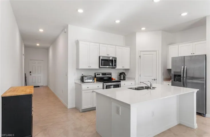 Kitchen featuring appliances with stainless steel finishes, an island with sink, white cabinets, recessed lighting, and butcher block countertops