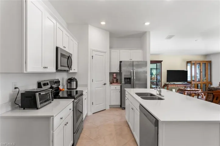 Kitchen featuring appliances with stainless steel finishes, white cabinetry, a center island with sink, open floor plan, and light stone counters