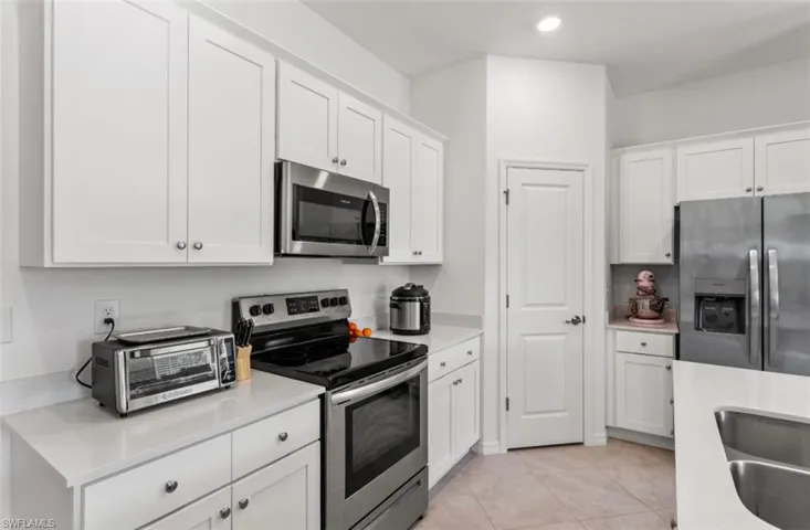 Kitchen with appliances with stainless steel finishes, white cabinetry, light tile patterned flooring, light stone countertops, and recessed lighting