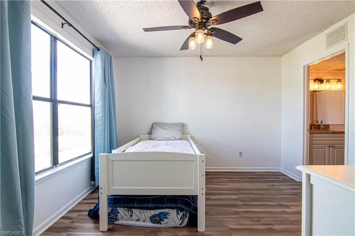 Bedroom with a textured ceiling, dark wood-style flooring, a ceiling fan, and connected bathroom