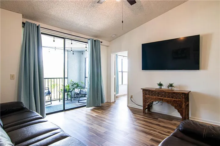 Living room with vaulted ceiling, wood finished floors, a textured ceiling, and ceiling fan