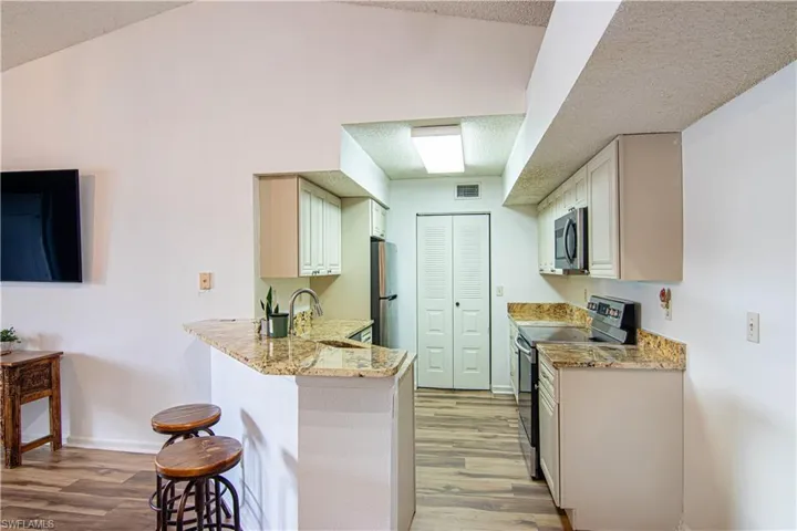 Kitchen featuring stainless steel appliances, light stone counters, a kitchen breakfast bar, light wood-style flooring, and a peninsula