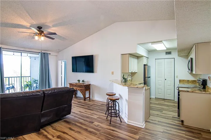 Kitchen with a textured ceiling, light stone counters, open floor plan, a kitchen breakfast bar, and vaulted ceiling