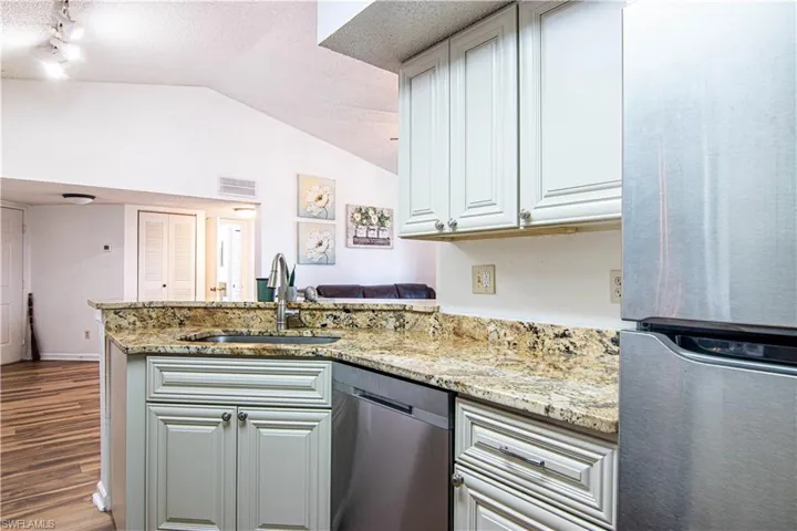 Kitchen with appliances with stainless steel finishes, a textured ceiling, light stone counters, vaulted ceiling, and a peninsula