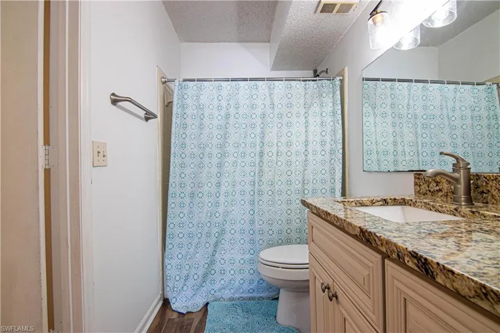 Full bathroom featuring a textured ceiling, curtained shower, vanity, and dark wood-type flooring