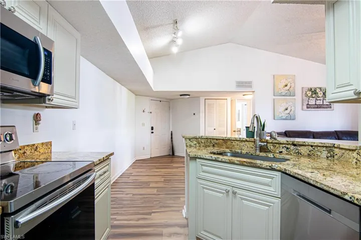 Kitchen featuring appliances with stainless steel finishes, a textured ceiling, light stone counters, dark wood-style flooring, and lofted ceiling