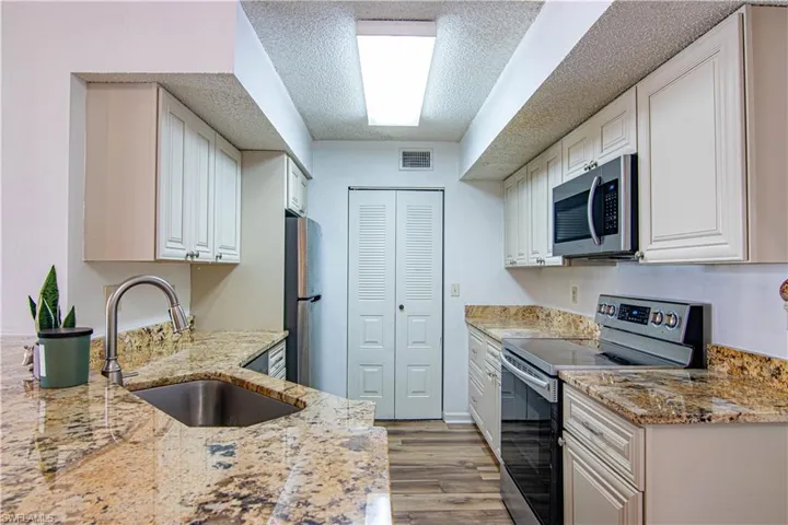 Kitchen with appliances with stainless steel finishes, light wood-style floors, light stone counters, a textured ceiling, and white cabinetry