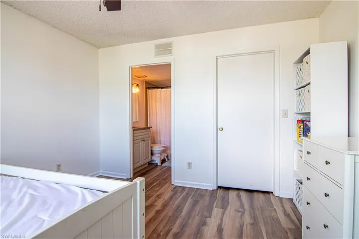 Unfurnished bedroom featuring a textured ceiling, dark wood-style floors, ceiling fan, and connected bathroom