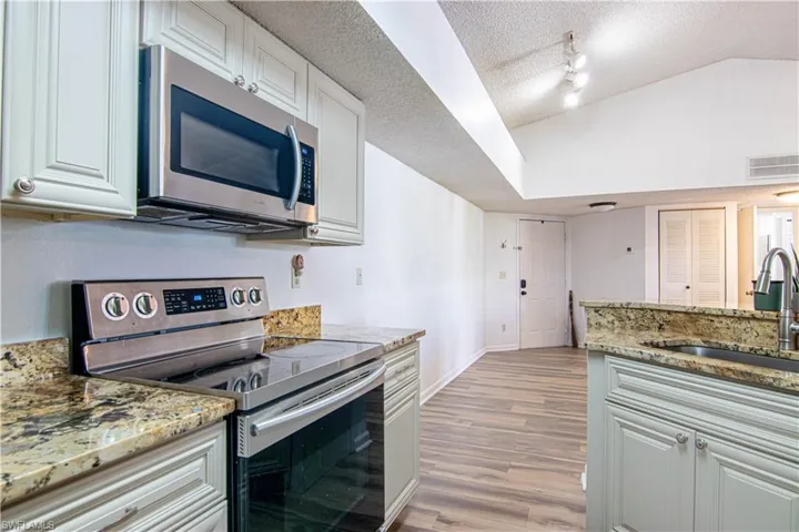 Kitchen with stainless steel appliances, light stone countertops, a textured ceiling, lofted ceiling, and light wood-style floors