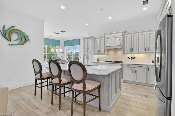 Kitchen with Level 8 Maple Alabaster Cabinets, pantry cabinet, breakfast bar, wine cooler, crown molding, and an island with sink
