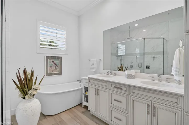 Bathroom with double vanity, crown molding, light wood-type flooring, a marble finish shower, and a freestanding bath