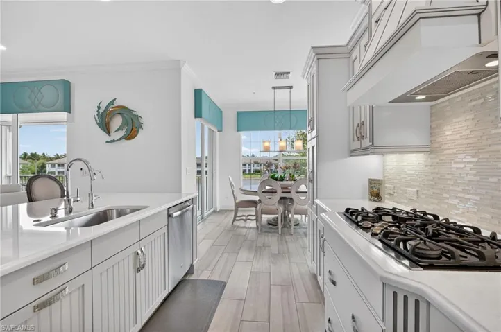 Kitchen with black gas stovetop, plank wood finish tile floors, light stone countertops, and dishwasher