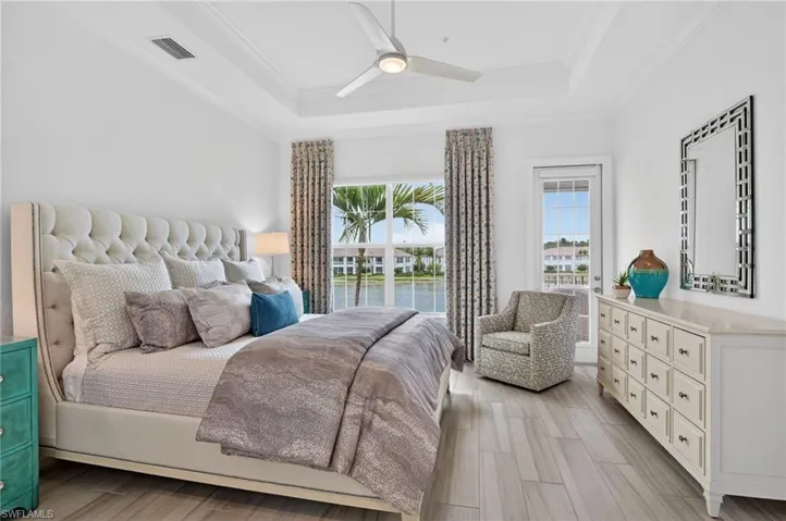 Bedroom featuring ceiling fan, wood finish floors, crown molding, a raised ceiling, and a water view