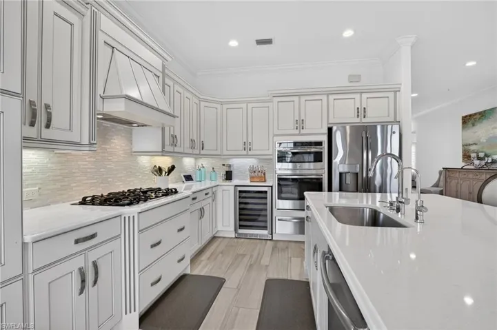 Custom Galley with beverage cooler, stainless steel appliances, crown molding, decorative backsplash, and light Quartz countertops