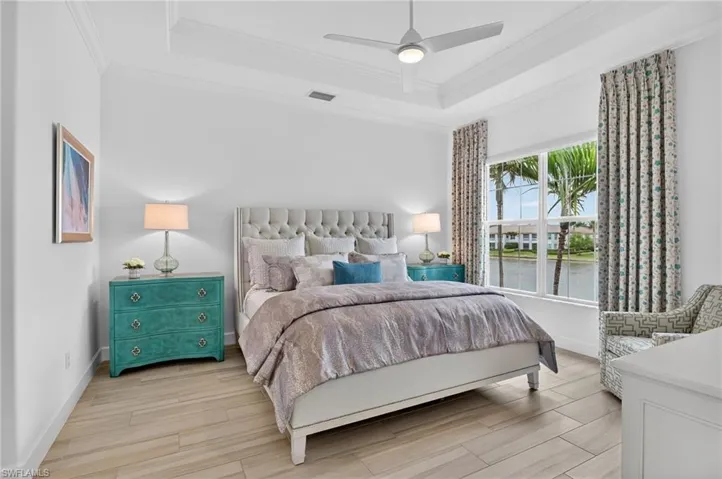 Primary Bedroom with wood finish floors, crown molding, ceiling fan, and a tray ceiling