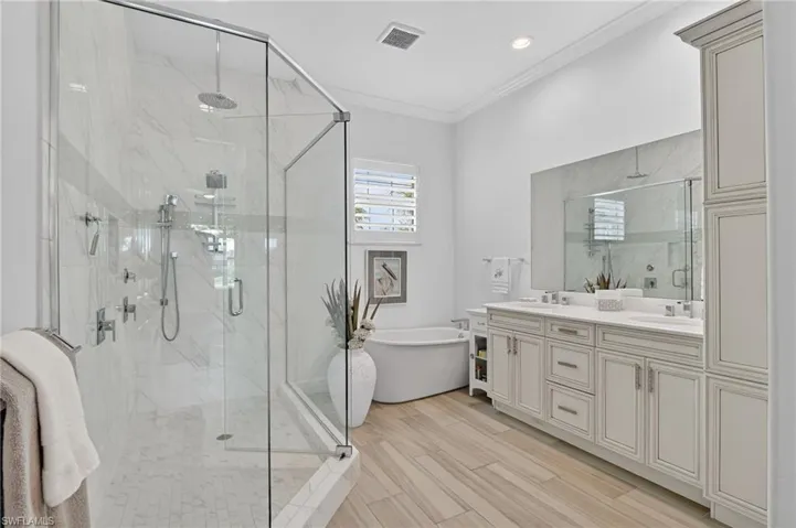 Full bath featuring double vanity, linen cabinet, a freestanding tub, crown molding, a marble finish shower, and light wood-type flooring