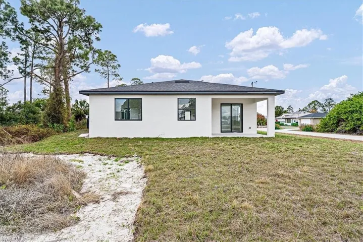 Rear view of house with stucco siding, a lawn, and a patio