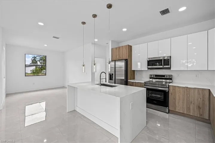 Kitchen featuring dual tone cabinetry, stainless steel appliances, decorative light fixtures, modern cabinets, and light stone countertops