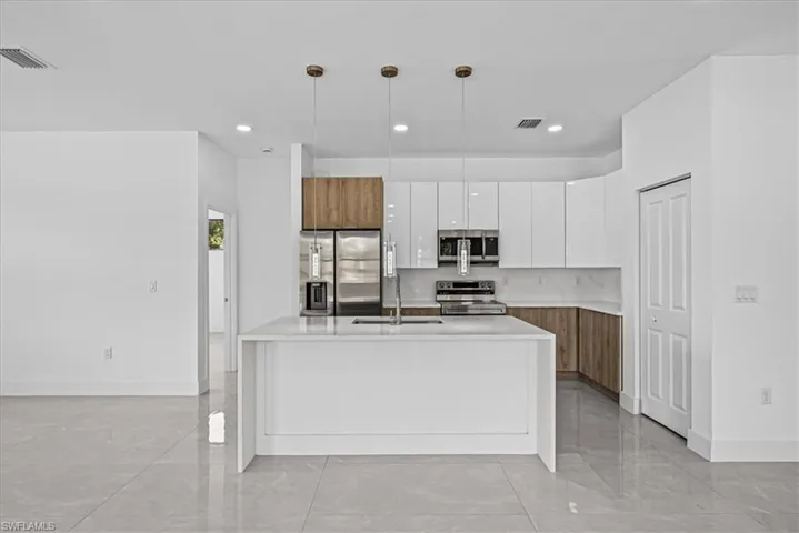 Kitchen with modern cabinets, dual tone cabinets, hanging light fixtures, stainless steel appliances, and light stone countertops