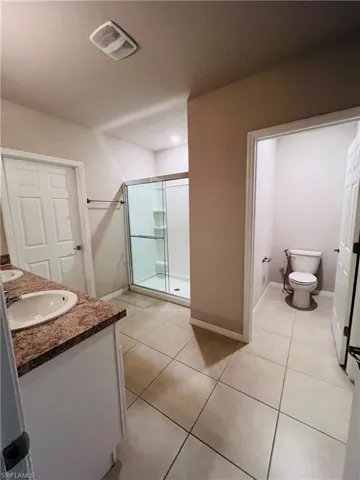 Full bath with double vanity, a stall shower, and light tile patterned flooring