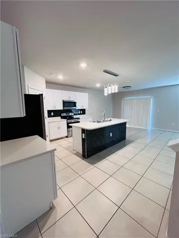 Kitchen featuring stainless steel appliances, light tile patterned floors, white cabinets, an island with sink, and decorative light fixtures