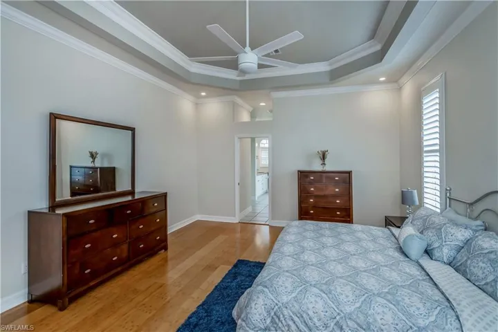 M-Bedroom with light bamboo flooring, a raised ceiling, ceiling fan, and crown molding