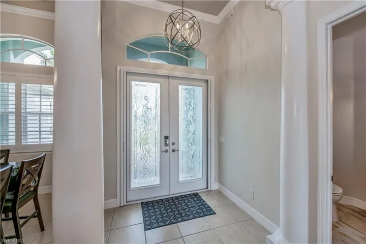 Foyer entrance featuring french doors, light tile patterned floors, a notable chandelier, and ornamental molding