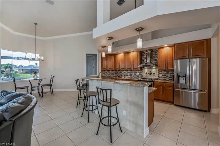 Kitchen featuring light stone countertops, appliances with stainless steel finishes, wall chimney range hood, light tile patterned floors, and hanging light fixtures
