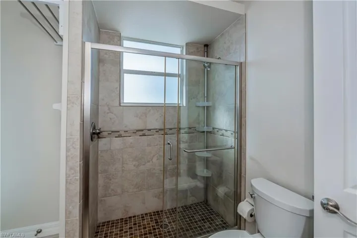 Bathroom featuring a shower with door and toilet