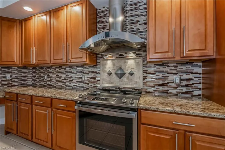 Kitchen featuring decorative backsplash, light tile patterned floors, electric range, and wall chimney range hood