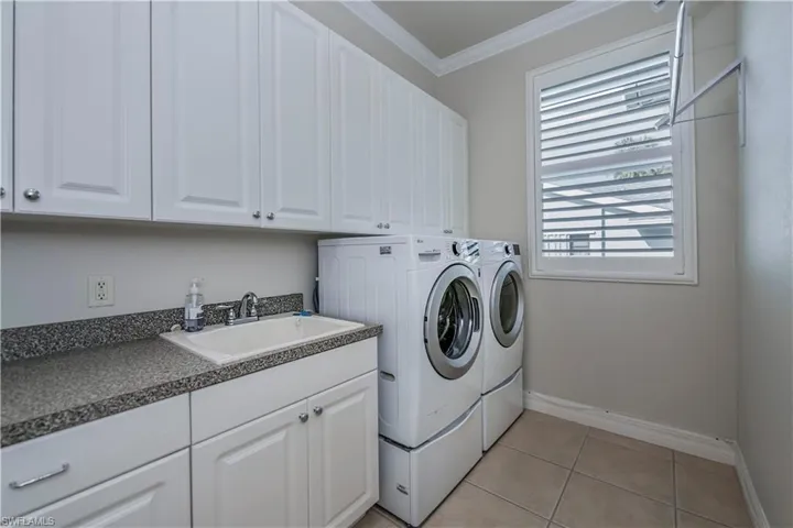 Laundry area with sink, cabinets, light tile patterned flooring, washer and dryer, and ornamental molding