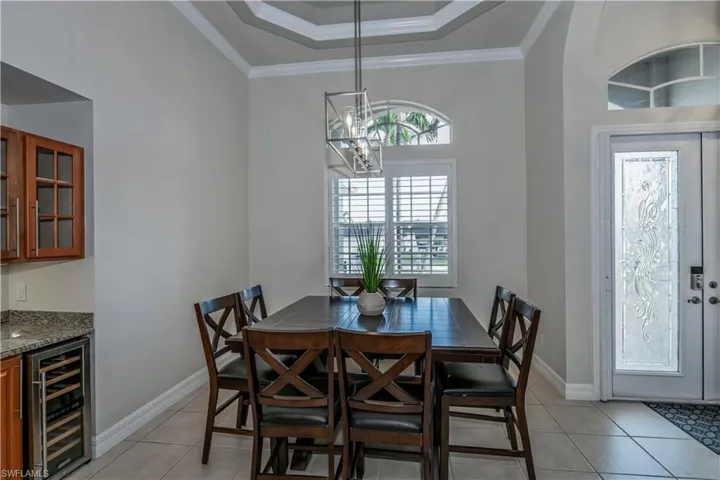 Tiled dining area featuring a chandelier, a raised ceiling, wine cooler, and crown molding