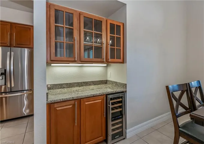 Bar with wine cooler, light stone countertops, light tile patterned flooring, and stainless steel refrigerator with ice dispenser