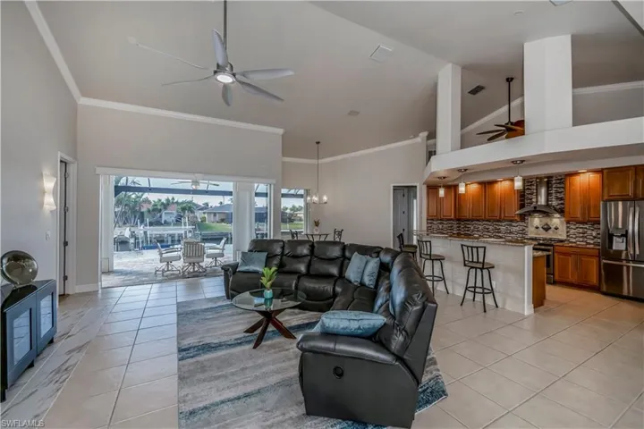 Living room featuring ceiling fan, light tile patterned flooring, crown molding, and high vaulted ceiling