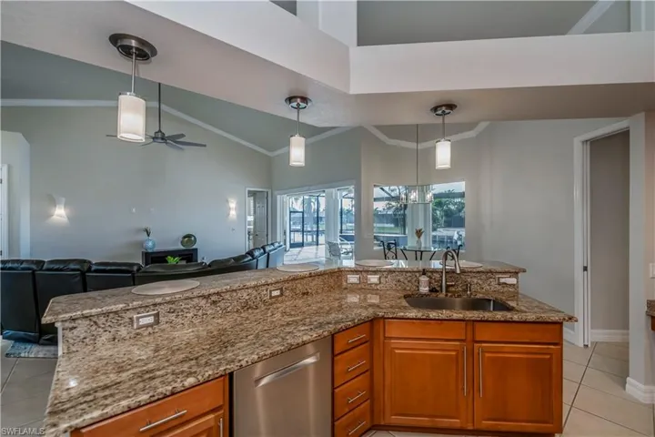 Kitchen with dishwasher, sink, pendant lighting, light tile patterned floors, and ceiling fan with notable chandelier