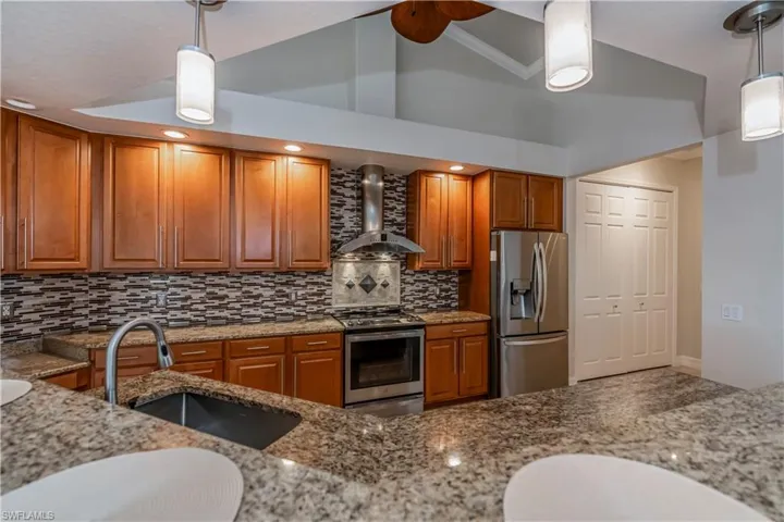 Kitchen featuring sink, wall chimney exhaust hood, light stone countertops, appliances with stainless steel finishes, and decorative light fixtures