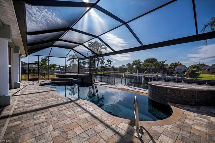 View of pool with glass enclosure, a patio area, a water view, and an in ground hot tub